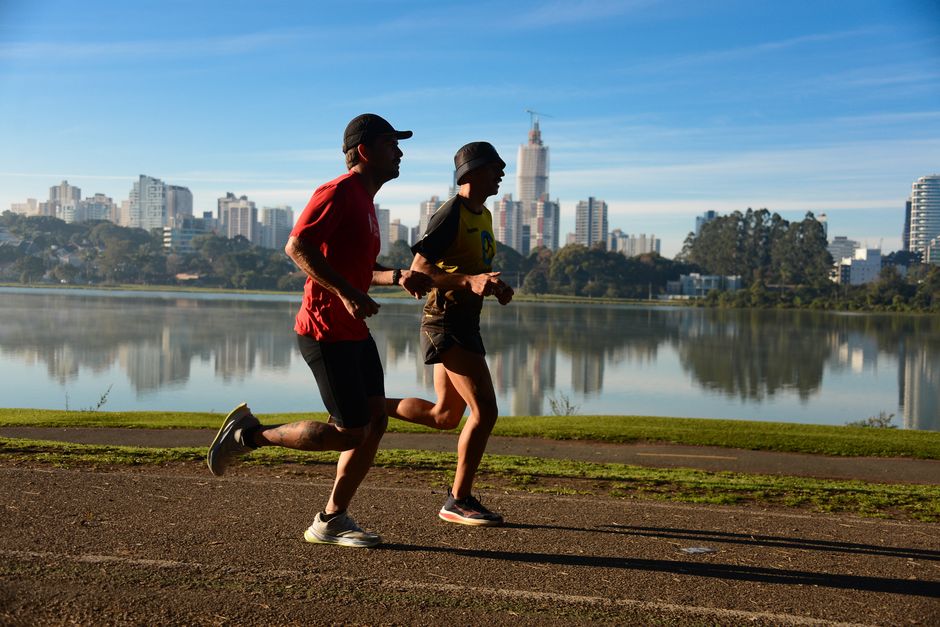 Imagem de duas pessoas correndo ao ar livre com vista para um lago e uma cidade ao fundo, ideal para artigos sobre saúde, bem-estar ou atividades físicas urbanas.
