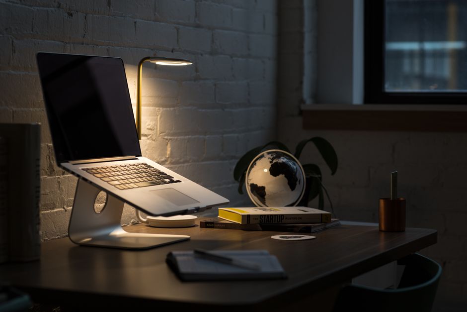 Ambiente de trabalho moderno com foco em empreendedorismo e planejamento estratégico, iluminado por uma luminária suave ao lado de um laptop, livros e objetos decorativos.
