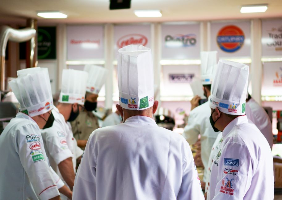 Chefes de cozinha participando de uma aula prática em uma escola de gastronomia, focada na preparação de pratos culinários.