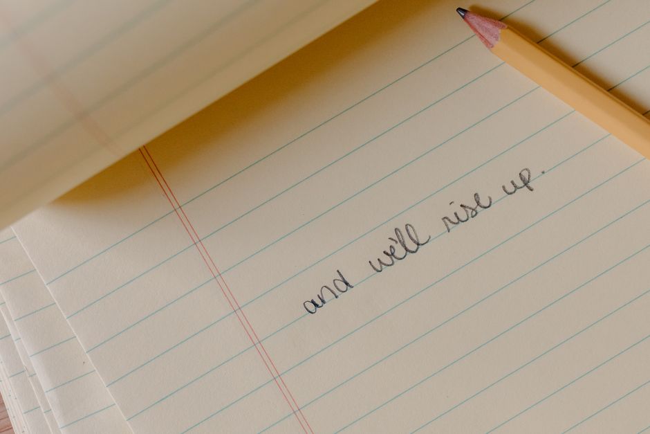 Página de caderno com a frase 'and we will rise up', acompanhada de lápis, simbolizando otimismo e motivação.