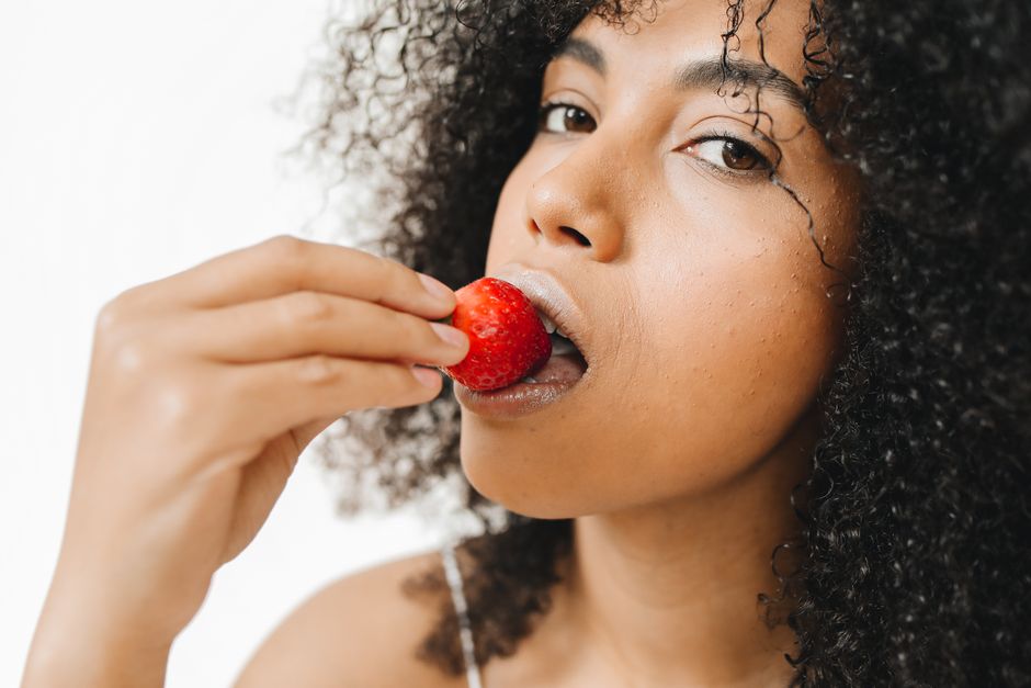 Mulher com cabelo encaracolado segurando uma morango, evocando temas de alimentação saudável e bem-estar.