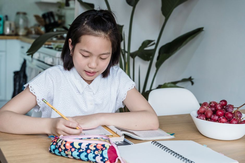 Jovem estudando em casa, com foco em tarefas escolares e organização do material de estudo.