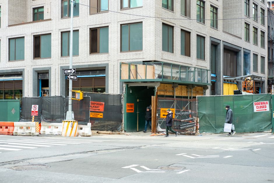 Construção de edifício comercial em andamento em uma área urbana com pedestres passando na calçada.