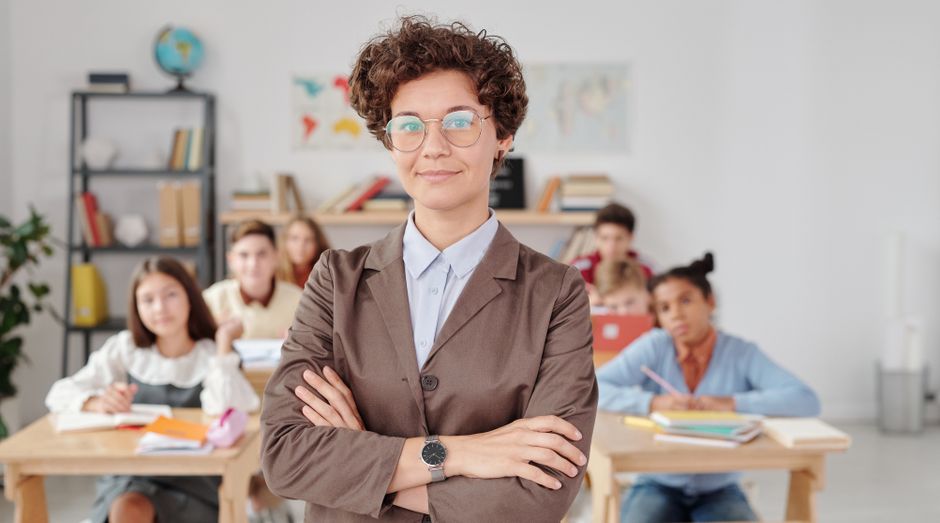 Professora segura os braços cruzados na sala de aula, transmitindo confiança para seus alunos.