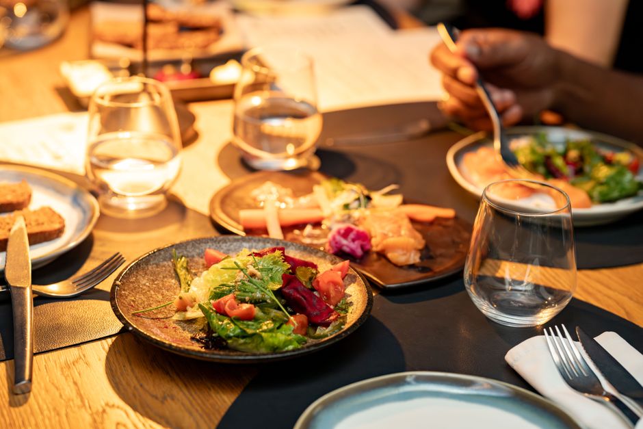 Imagem de uma mesa de jantar com pratos de salada, sashimi e bebidas, ideal para ilustrar um artigo sobre culinária, gastronomia ou experiências gastronômicas em restaurantes.