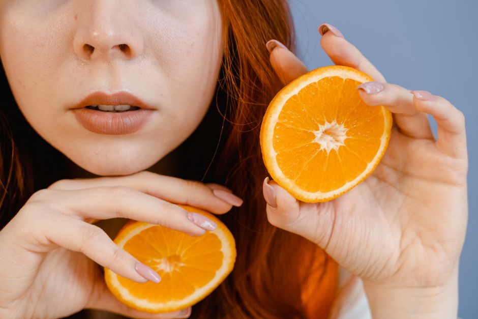 Mulher com cabelo ruivo segurando duas fatias de laranja, representando saúde e nutrição natural.