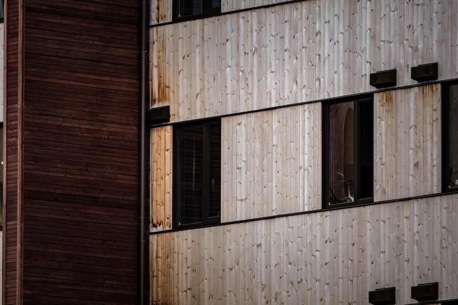 Imagem de fachada de edifício com revestimento de madeira, destacando a estética de arquitetura moderna com janelas pretas e iluminação externa.