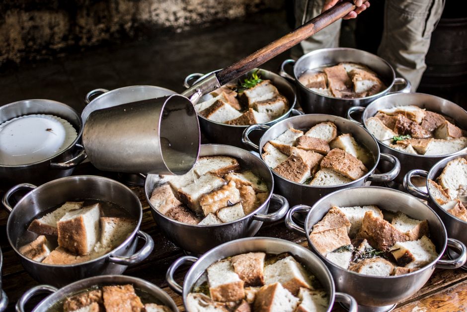 Imagem de diversas panelas contendo pedaços de pão embebidos em leite, evocando uma preparação culinária tradicional de sobremesas ou café da manhã.