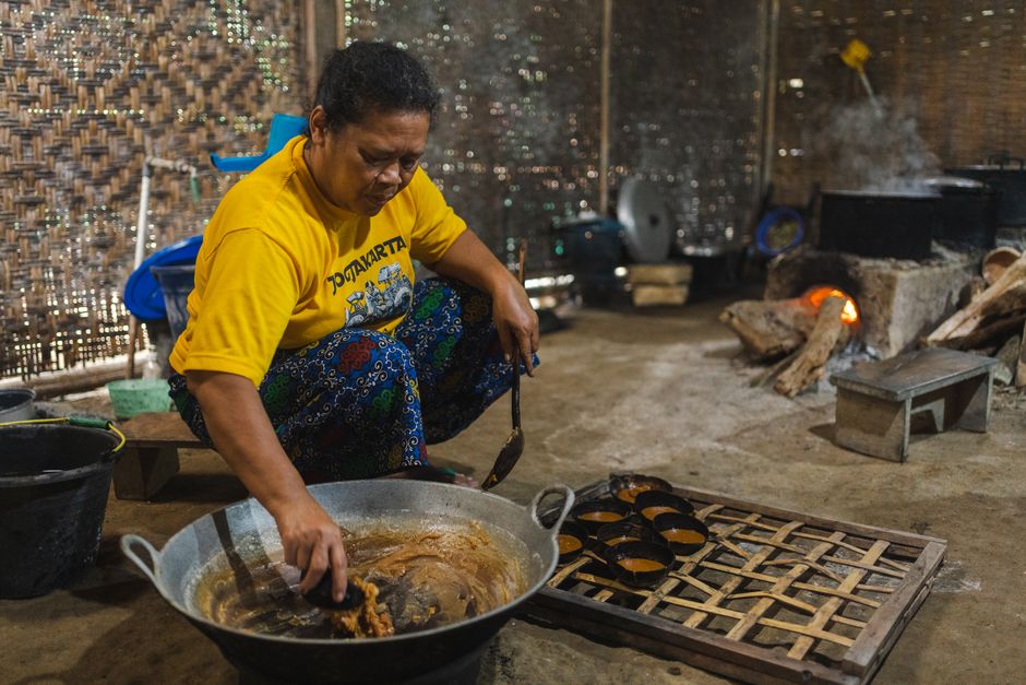 Mulher preparando comida tradicional em uma cozinha de alvenaria com forno a lenha, transmitindo cultura e processo artesanal de culinária.