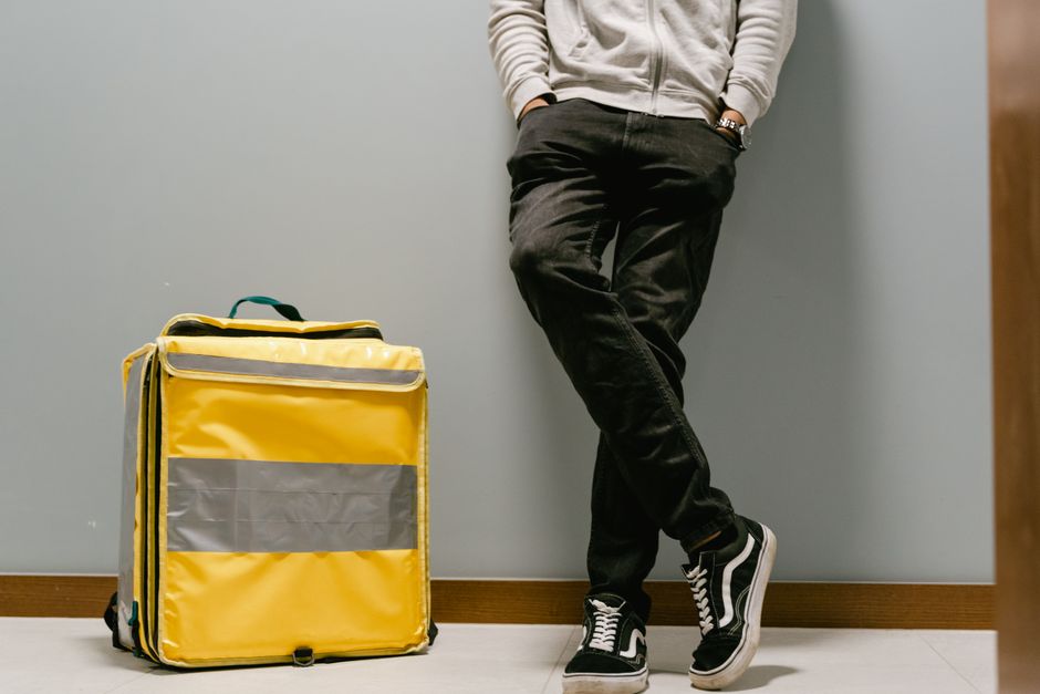 Pessoa de costas aguardando com uma mochila amarela em ambiente interno, simbolizando viagem ou transporte.