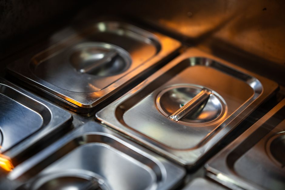 Imagem de recipientes de aço inox, típicos de uma cozinha industrial, sugerindo foco em alimentos, gastronomia ou serviço de restaurante.