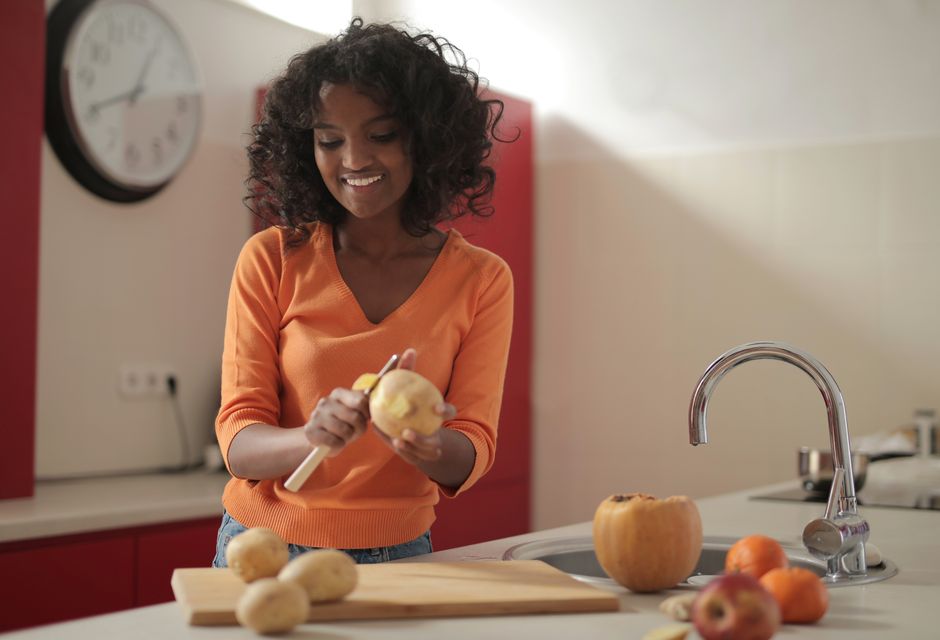 Mulher sorridente descascando uma maçã no ambiente de uma cozinha moderna, preparando ingredientes para uma receita.