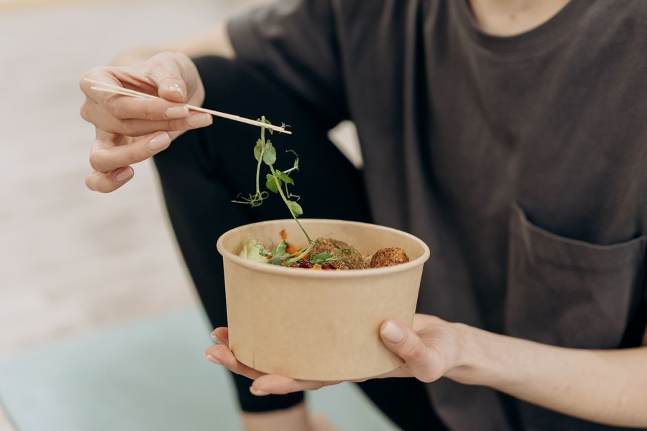 Pessoa segurando uma tigela de comida saudável enquanto adiciona ervas, representando alimentação saudável e bem-estar.