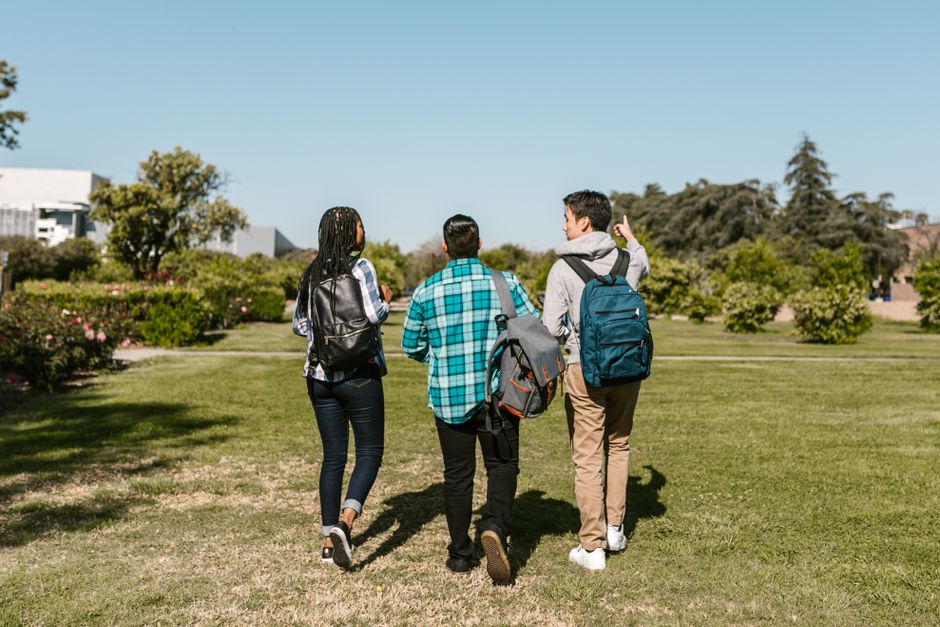 Grupo de jovens caminhando ao ar livre, envolvido em uma conversa descontraída, em um parque sob céu claro.