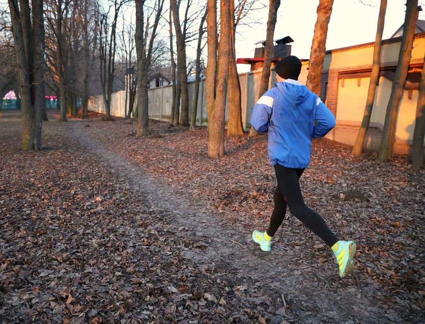 Pessoa praticando corrida ao ar livre em um ambiente natural com árvores e trilha na natureza durante o fim de tarde.