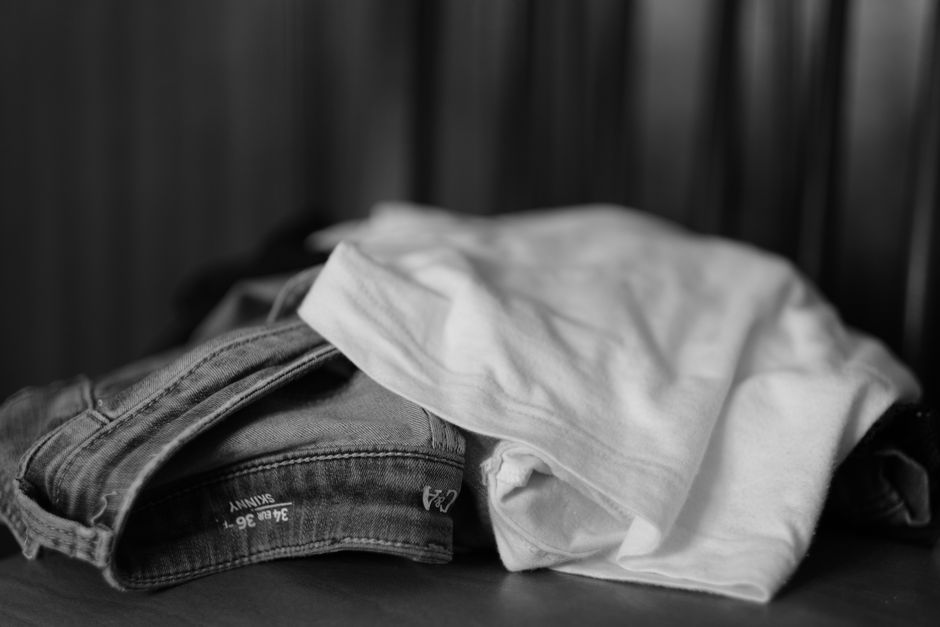 Imagem de roupas como jeans e camisetas desalinhadas sobre uma superfície, transmitindo uma sensação de casualidade e cotidiano.