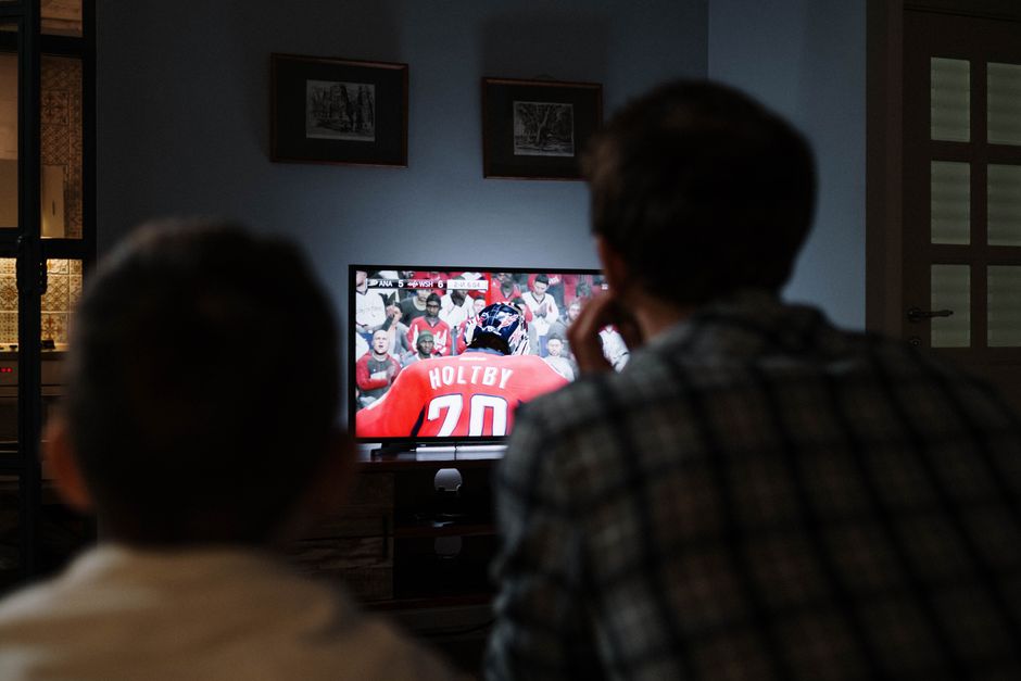 Dois adultos assistindo a um jogo de hóquei na televisão em um ambiente acolhedor, destacando a participação em eventos esportivos em casa.