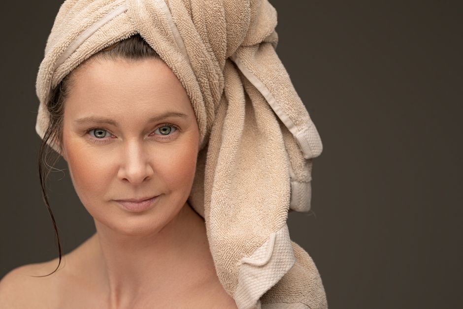 Mulher com toalhas na cabeça, aparentando relaxamento e cuidados pessoais, ideal para conteúdo sobre beleza ou bem-estar.