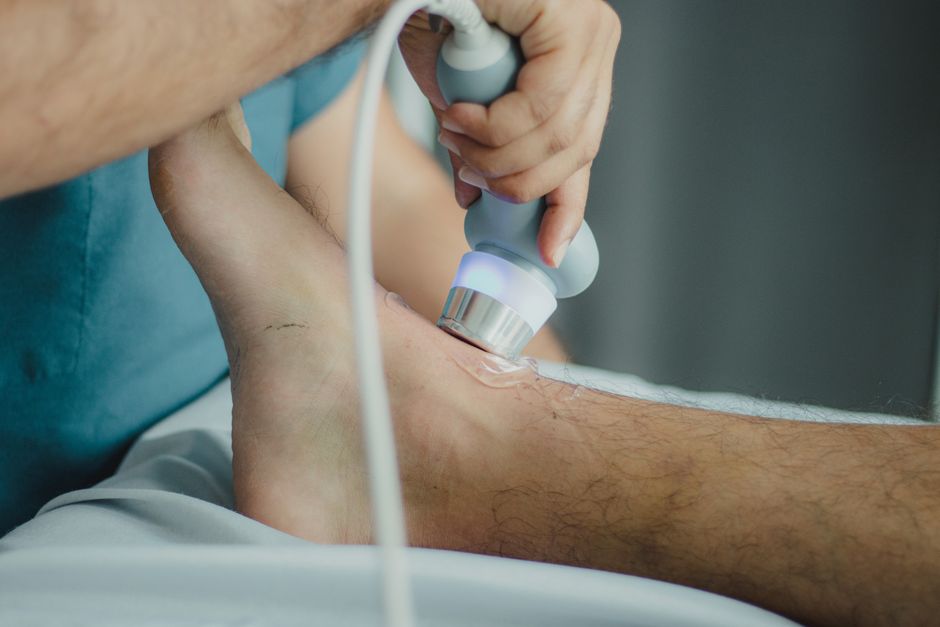 Profissional realizando um procedimento de ultrassonografia na região do tornozelo, indicativo de avaliação médica ou tratamento ortopédico.