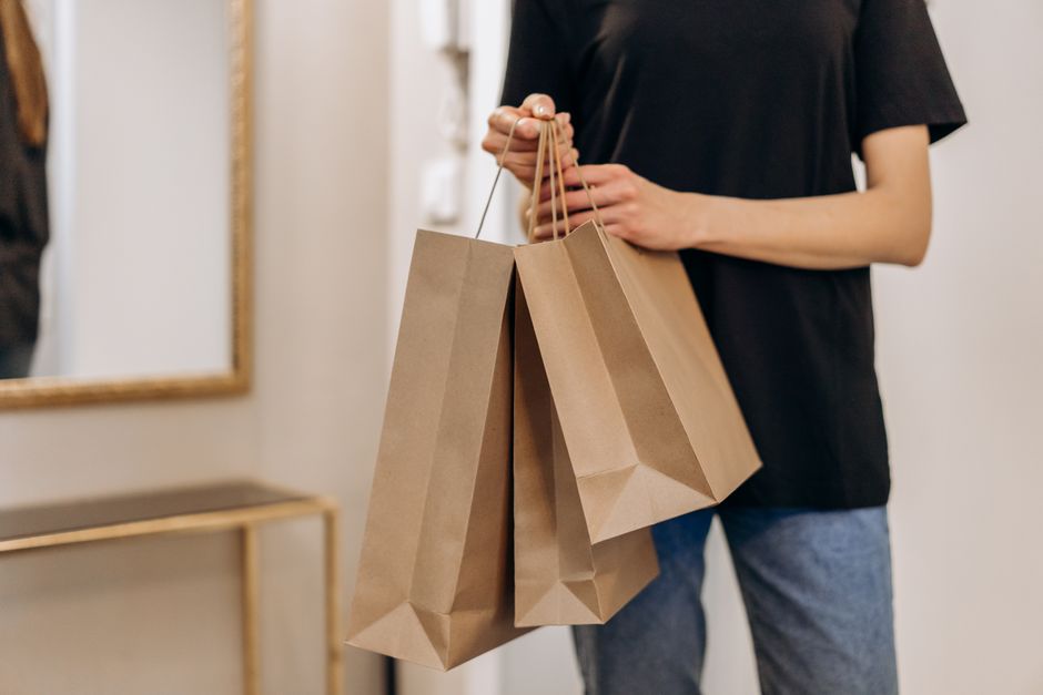 Pessoa segurando sacolas de compras de comércio varejista em um ambiente interno, representando consumo e compras sociais.