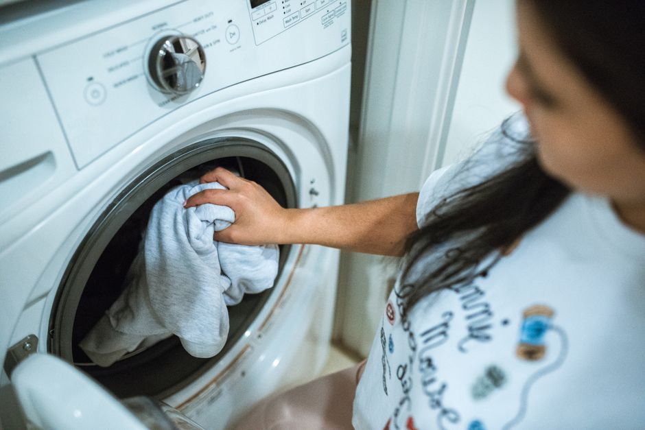 Mulher colocando roupas na máquina de lavar, simbolizando tarefas domésticas e gestão do lar.