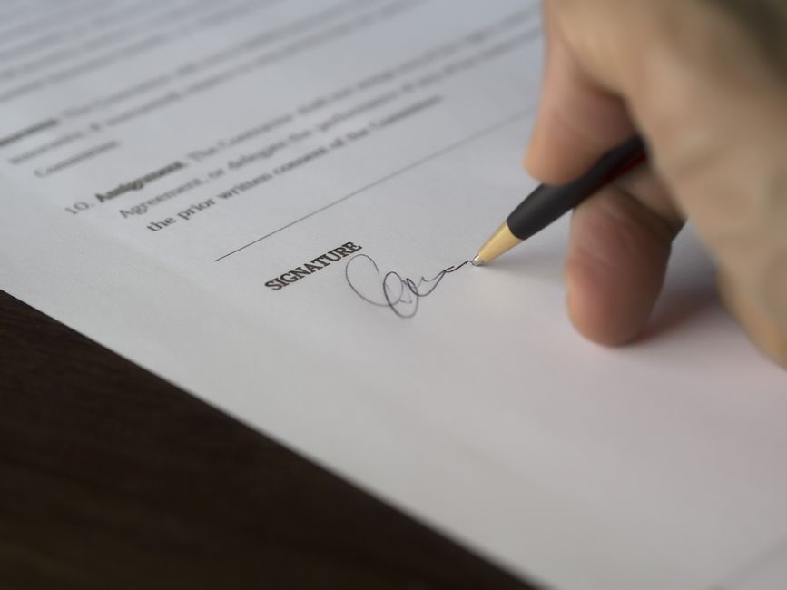 Pessoa assinando um documento formal, simbolizando acordo ou formalização de negócios.