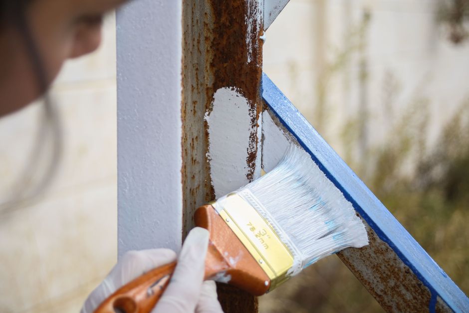 Pessoa pintando uma superfície de ferro enferrujada com pincel na área de manutenção ou reparos.