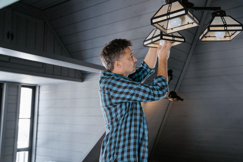 Homem ajustando a iluminação em um espaço com teto de madeira, ideal para ilustrar renovação ou decoração de interiores.