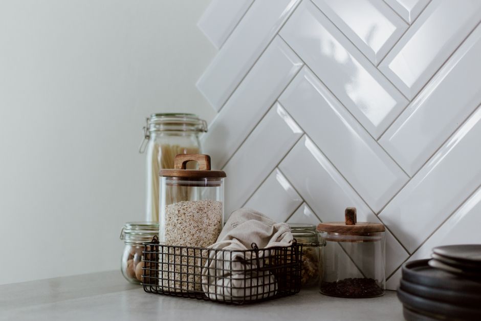 Imagem de uma cozinha moderna com recipientes de vidro e uma pia de azulejos brancos, sugerindo organização e praticidade na rotina doméstica.