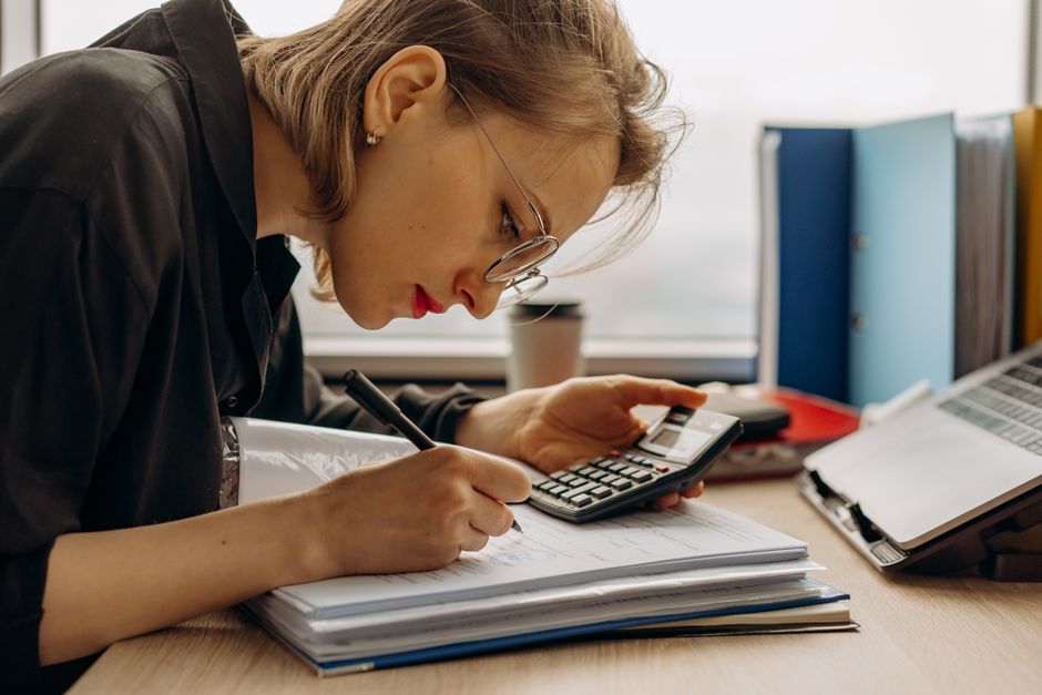 Mulher concentrada realizando cálculos e análise de dados em ambiente de trabalho de escritório.
