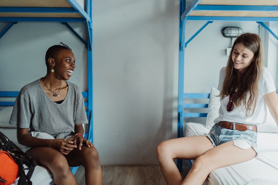 Duas jovens mulheres conversando e sorrindo em um ambiente informal com beliche azul ao fundo.