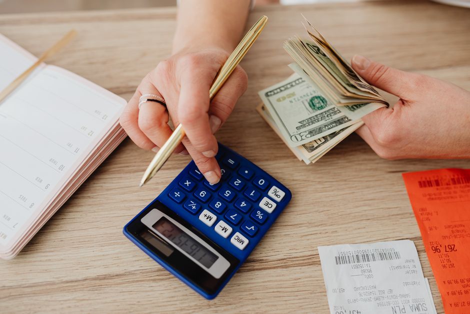 Pessoa manipulando dinheiro, usando uma calculadora e anotando dados, simbolizando planejamento financeiro ou controle de gastos.