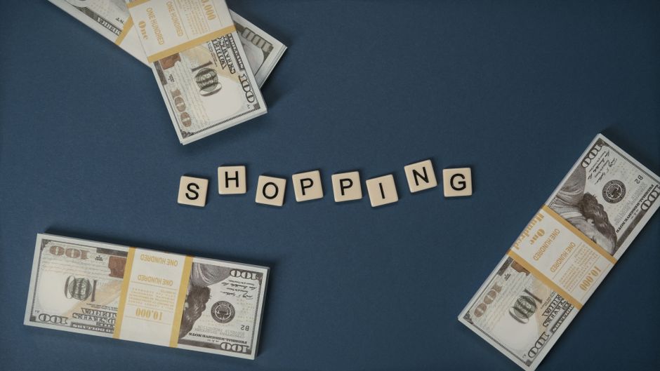 Imagem que representa o tema de compras financeiras, destacando pacotes de dinheiro em meio a letras que formam a palavra 'shopping', ideal para artigos sobre consumo ou gestão financeira pessoal.
