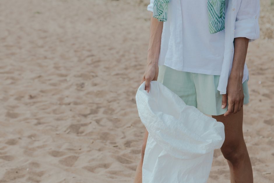 Pessoa segurando uma sacola de papel na areia, evocando uma temática de consumo consciente ou sustentabilidade na praia.