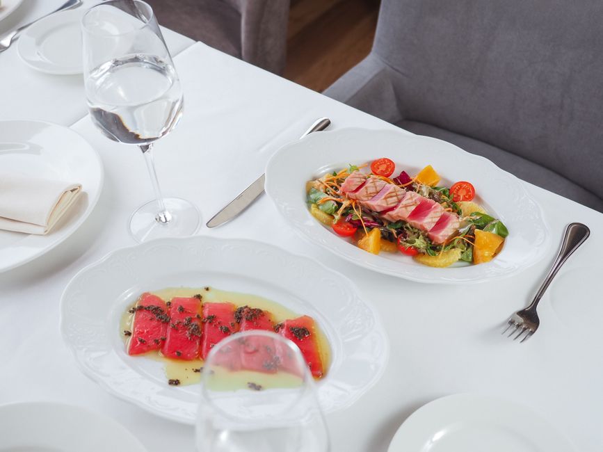Imagem de uma mesa de restaurante com pratos gourmet, utensílios e taças de água, sugerindo um momento de refeição refinada ou uma experiência gastronômica sofisticada.
