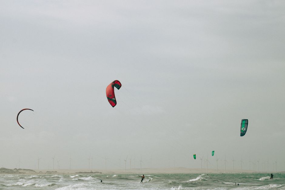 Capa de blog sobre esportes aquáticos, mostrando pessoas praticando kite surf na orla marítima sob céu nublado.
