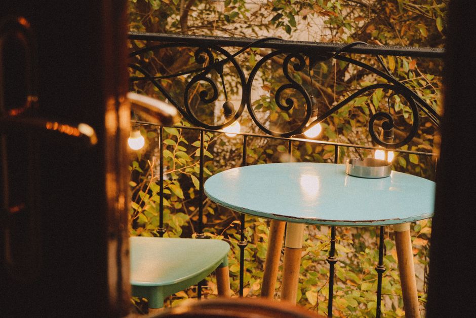 Imagem de um espaço ao ar livre com uma mesa azul e cadeiras em um ambiente acolhedor, perfeito para momentos de descanso ou encontros informais durante o pôr do sol.