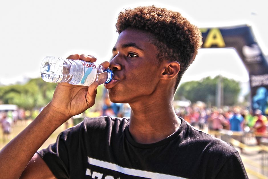 Jovem bebendo água após uma corrida ou atividade física ao ar livre, simbolizando saúde e bem-estar em eventos esportivos.