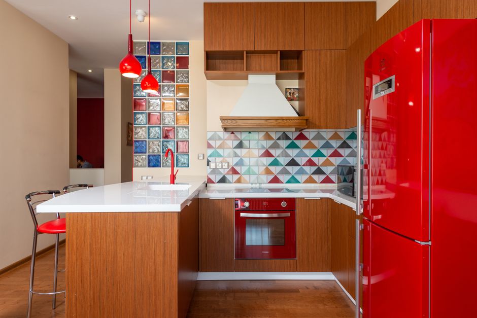 Cozinha moderna com armários de madeira, backsplash decorativo e eletrodomésticos vermelhos, destacando o design contemporâneo e colorido do ambiente.