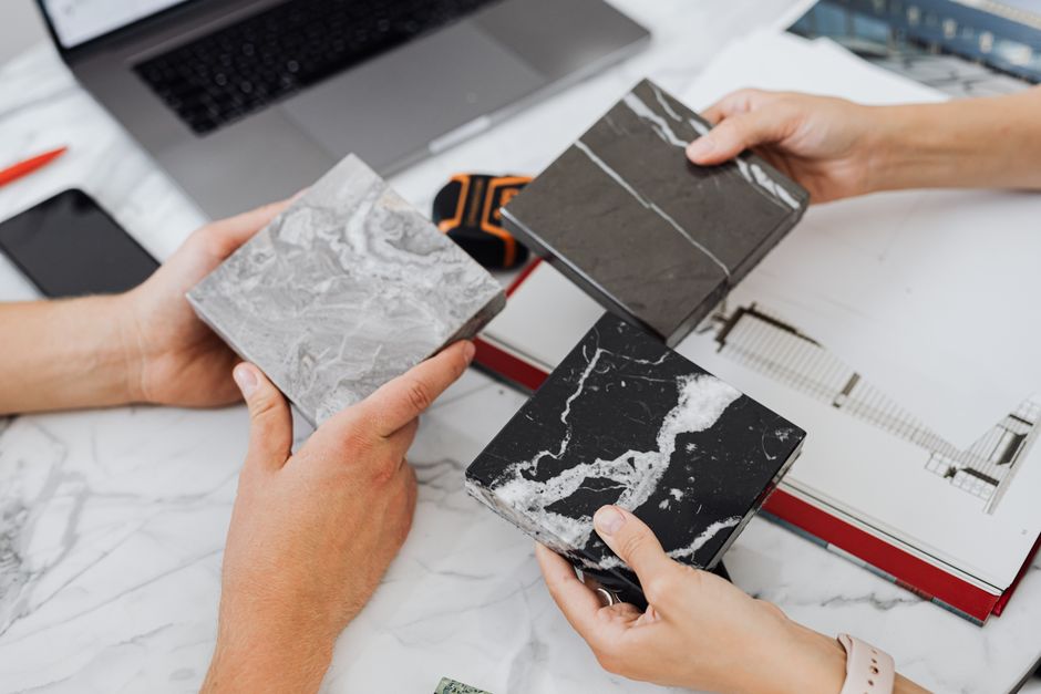 Duas pessoas trocando amostras de mármore em um ambiente de trabalho, indicando uma discussão sobre materiais de acabamento para projetos de decoração ou construção.