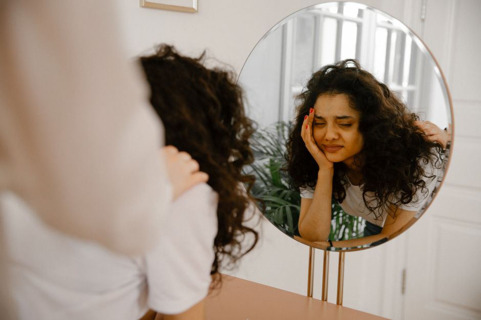Mulher olhando para o espelho com expressão de preocupação, refletindo questões de autoestima ou ansiedade.