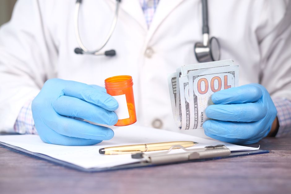 Médico colocando medicamentos e dinheiro sobre uma mesa, simbolizando aspectos relacionados à saúde financeira ou custos na área da saúde.
