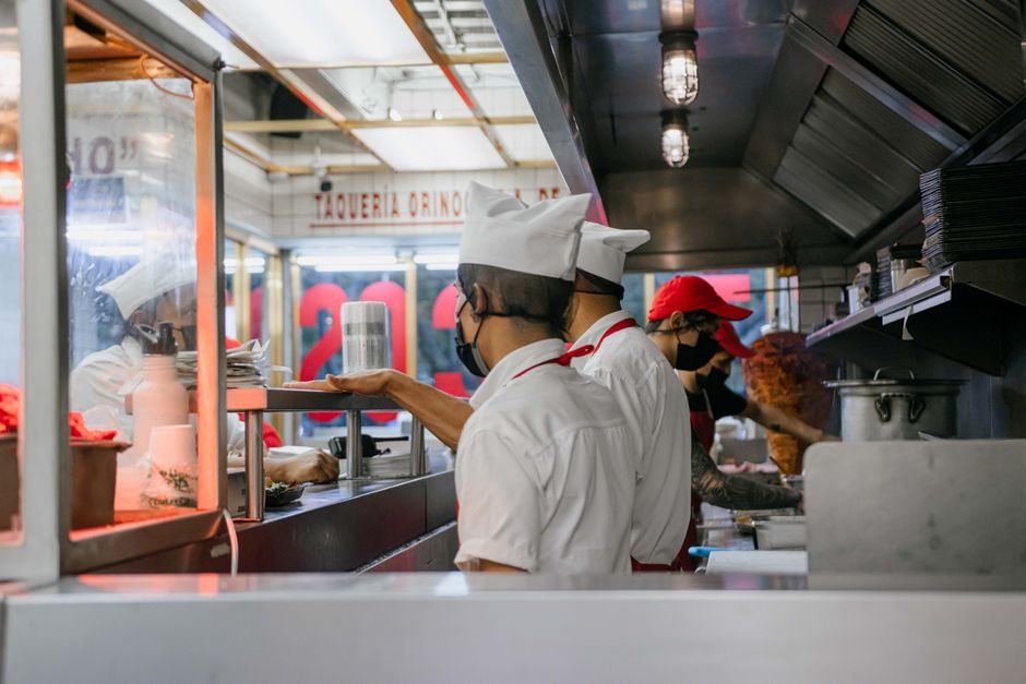 Equipe de cozinheiros preparando alimentos em uma cozinha de restaurante com foco na organização e no trabalho em equipe.