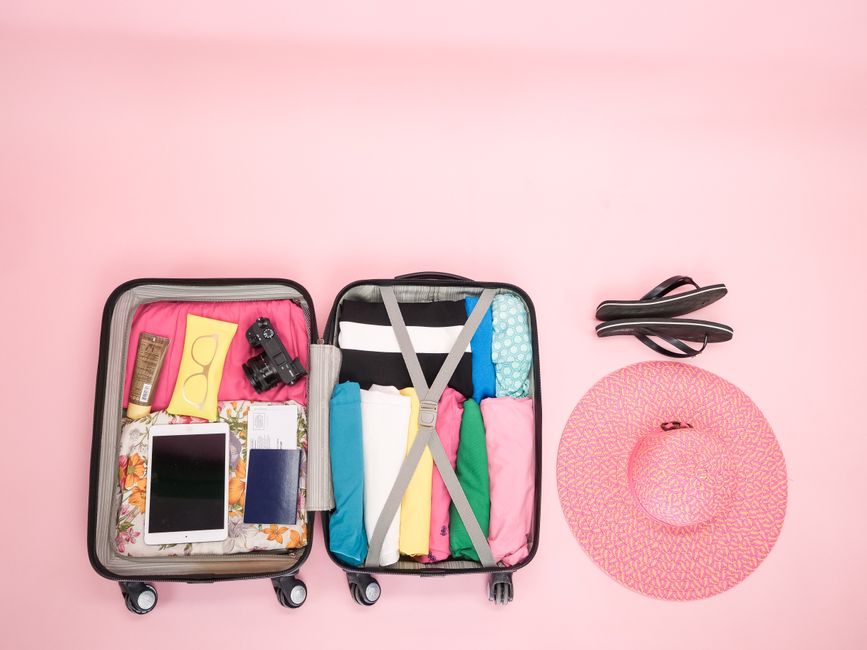 Mala de viagem aberta com roupas e itens de uso pessoal organizados, pronta para uma viagem, com acessórios ao lado.
