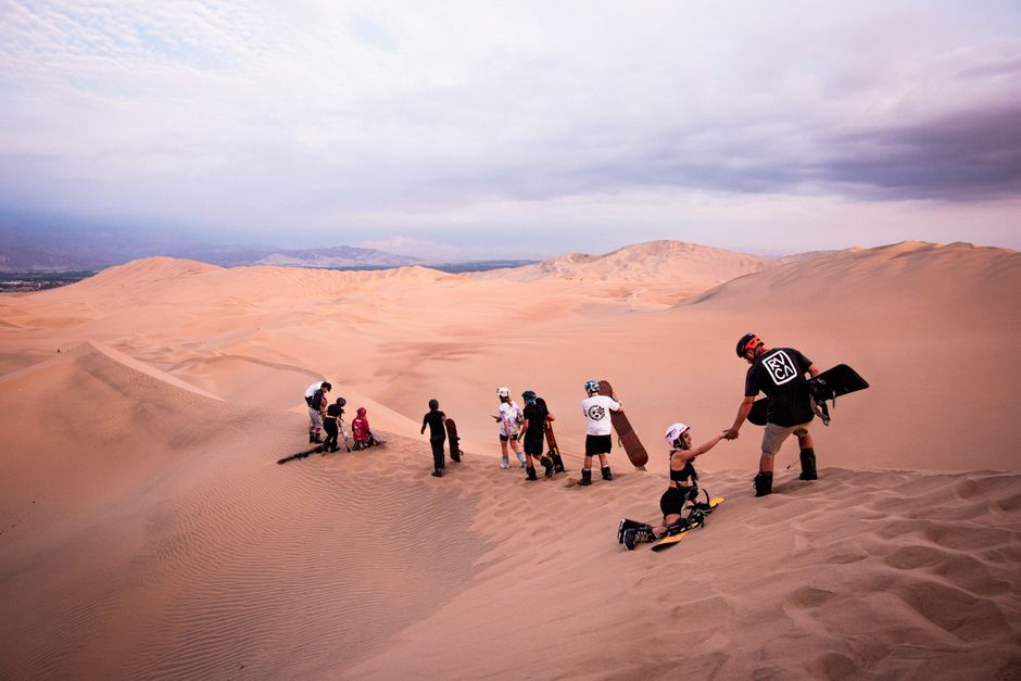 Grupo de pessoas, incluindo crianças, explorando dunas de areia ao entardecer em uma aventura ao ar livre, com caminhadas e atividades de lazer na natureza.