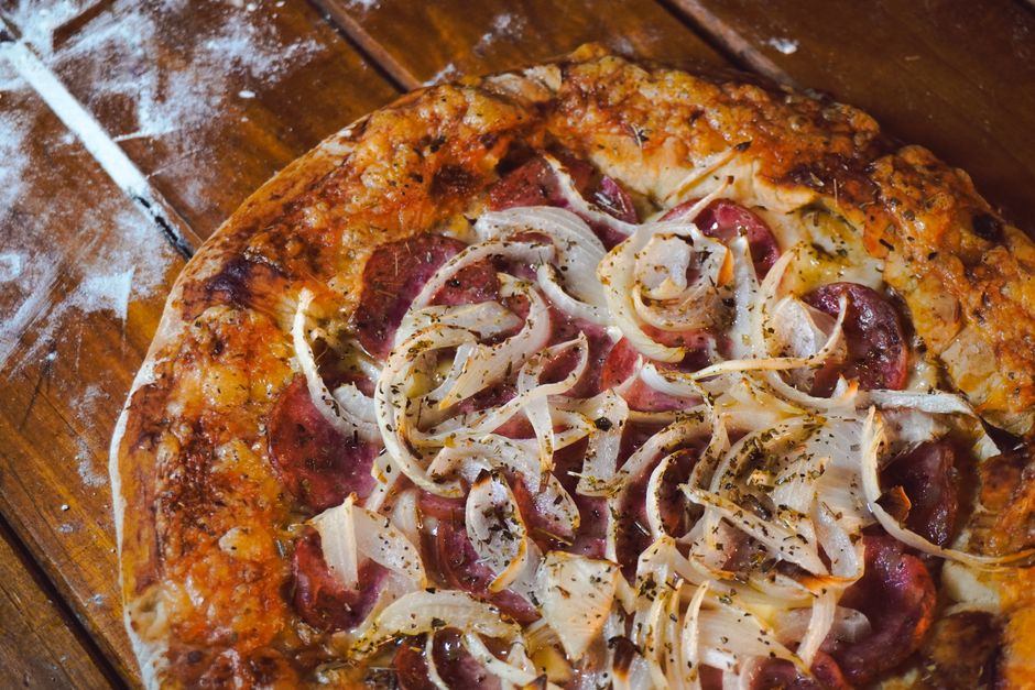Pizza artesanal com queijo, cebola e linguiça em uma mesa de madeira, ideal para um artigo sobre culinária e gastronomia italiana.