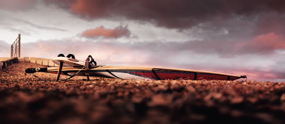 Imagem de uma prancha de stand-up paddle deitada na orla, destacando o cenário ao pôr do sol, ideal para artigos sobre esportes aquáticos ou lazer ao ar livre.