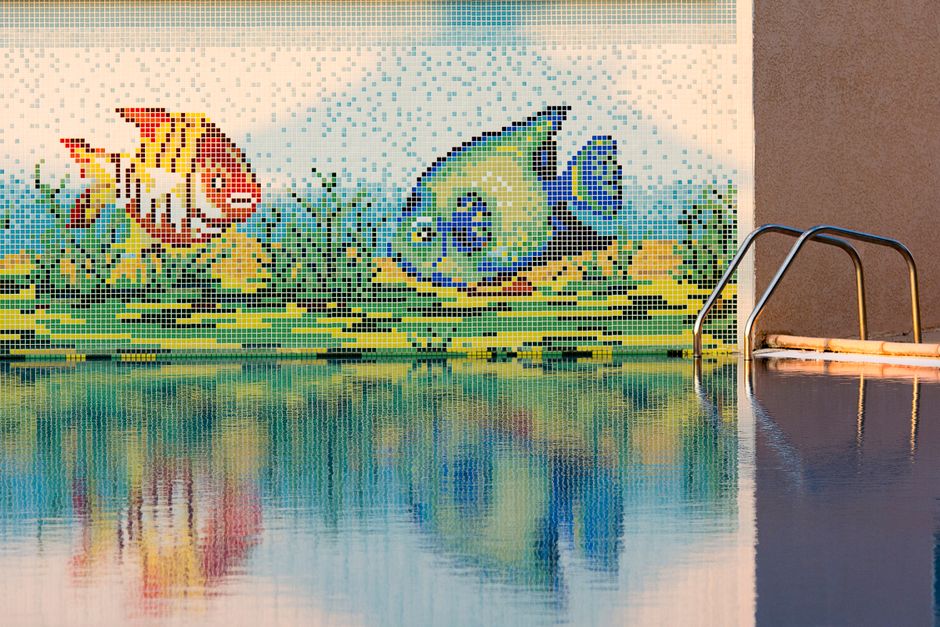 Imagem de uma parede decorada com mosaico de peixes coloridos ao lado de uma piscina, criando um ambiente aquático e vibrante.