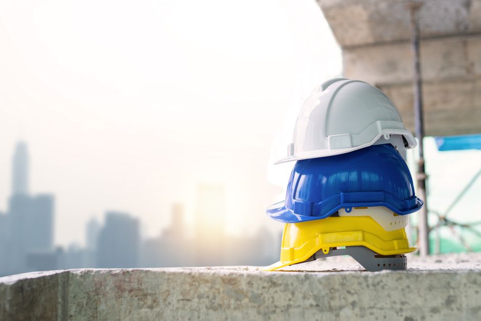Imagem de capacetes coloridos empilhados em um canteiro de obras, simbolizando segurança na construção civil e trabalho em equipe.
