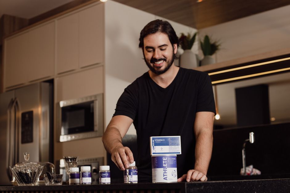 Homem sorridente preparando vitaminas no ambiente da cozinha com um estilo contemporâneo e acolhedor.